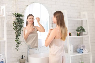 Sivilceli genç bir kadın banyoda aynanın yanında serum takıyor.