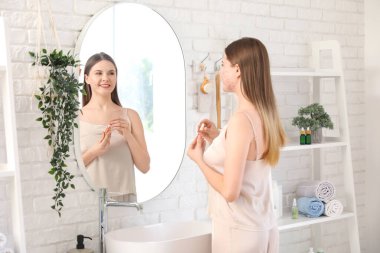 Sivilceli genç bir kadın ve banyoda aynanın yanında serum.