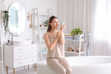 Sivilceli genç bir kadın ve banyoda cilt ürünleri.
