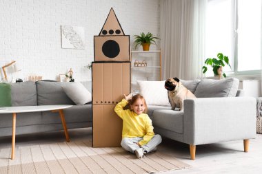 Evde karton roket ve köpek oynayan küçük bir kız.