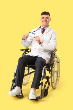 Tekerlekli sandalyedeki genç erkek doktor. Sarı arka planda isim etiketi yok.