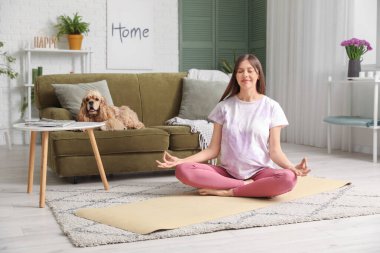 Cocker spaniel ile evde meditasyon yapan genç ve sportif bir kadın.