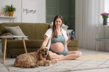 Cocker spaniel ve su şişesiyle evde yoga yapan genç ve sportif bir kadın.