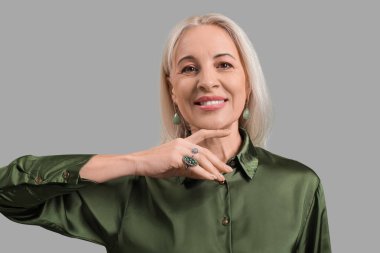 Gri arka planda güzel küpeleri ve yüzükleri olan mutlu olgun bir kadın.
