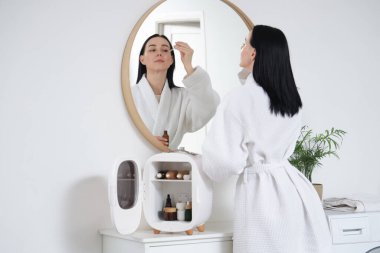 Banyoda serumu ve kozmetik buzdolabı olan genç bir kadın.