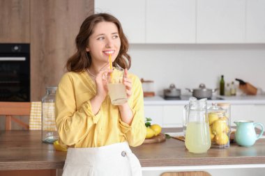 Genç bayan mutfakta limonata içiyor.