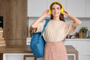 Mutfakta sırt çantalı kulaklıklı mutlu bayan öğrenci.