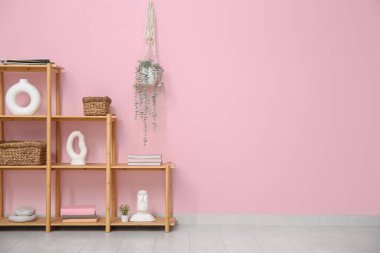 Dekorlu raf ünitesi ve pembe duvarın yanında asılı ev bitkisi.