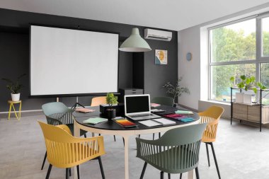 Masa ve projektör ekranlı konferans odasının içi