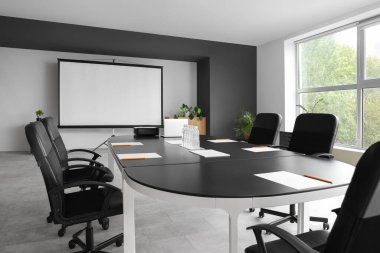 Masa ve projektör ekranlı konferans salonunun içi