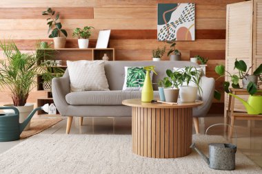 Oturma odasının içinde kanepe, yeşil bitkiler ve bahçe aletleri var.