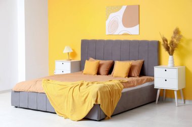 Rahat yataklı, komodinli, lamba ve vazo dolusu otlu güzel bir yatak odası.