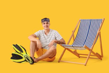 Sarı arka planda oturan şnorkel maskeli genç adam.