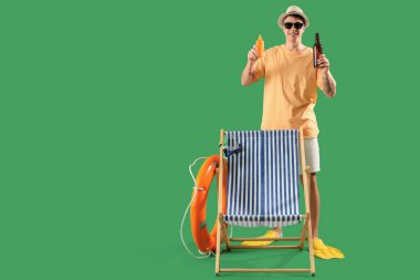 Yeşil arka planda güneş kremi ve bira olan genç bir adam.