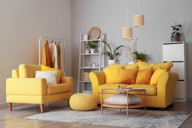 Oturma odasının içinde sarı kanepe, koltuk ve yeşil bitkiler var.