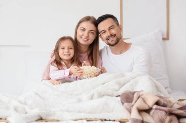 Patlamış mısırlı küçük bir kız ve ailesi yatak odasında film izliyor.
