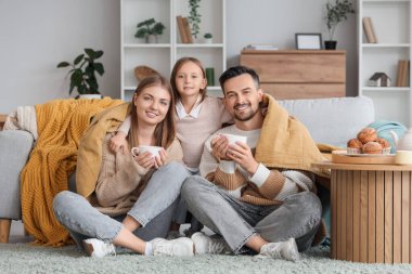 Küçük kız sıcak ekose kumaş ve çay eşliğinde ailesine sarılıyor.