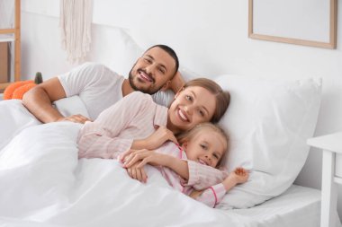 Mutlu ebeveynler ve küçük kızları yatak odasında yumuşak bir battaniyenin altında yatıyor.
