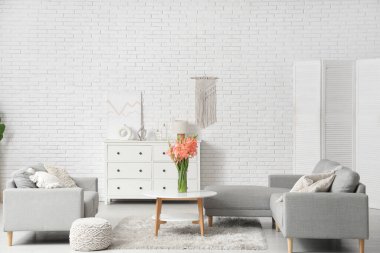 Oturma odasının içinde kanepeler ve vazoda gladiolus çiçekleri var.