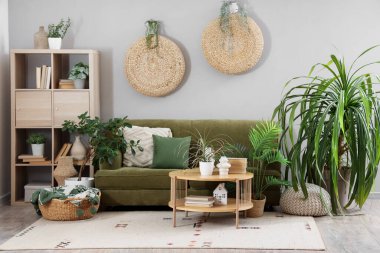 Oturma odasının içinde yeşil kanepe, masa ve bitkiler var.