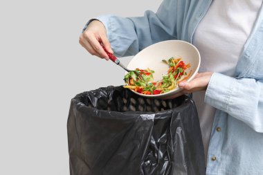 Arka plandaki çöp kutusuna organik yiyecek atan genç bir kadın, yakın plan. Atık geri dönüşüm kavramı