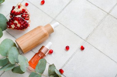 Temel yağ, nar ve okaliptüs şişeleriyle hafif fayans arkaplan üzerine kompozisyon