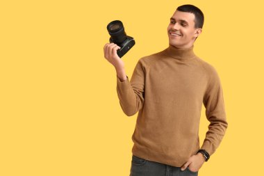 Sarı arka planda modern kameralı bir erkek fotoğrafçı.