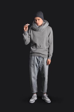 Koyu arkaplanda termometresi olan hasta genç bir adam.