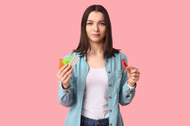 Doğum kontrol hapları, kırmızı kurdele ve pembe arka planda prezervatifleri olan güzel bir genç kadın. AID farkındalık kavramı