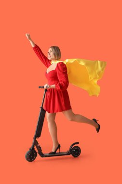 Turuncu arka planda süper kahraman pelerini ve scooter 'ı olan güzel olgun bir kadın.