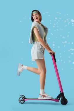 Mavi arka planda sabun köpüğü süren mutlu genç bir kadın.