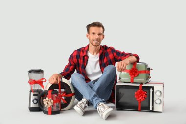 Handsome man with gift appliances sitting on grey background clipart