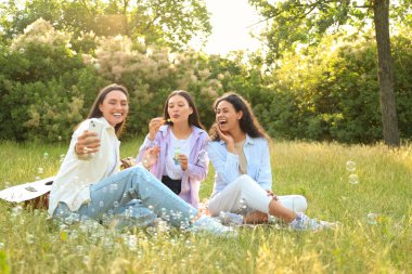 Sabun köpüklü genç kadınlar parkta piknik yaparken selfie çekiyorlar.