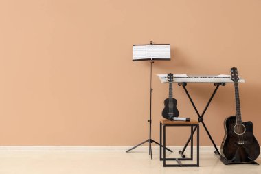 Farklı gitarlar, sentezleyici ve bej duvarın yanında duran müzik notaları.