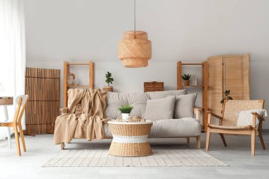 Koltuk, koltuk, yuvarlak masa, ev bitkisi ve bavul oturma odasının iç tarafındaki hasır tepside.