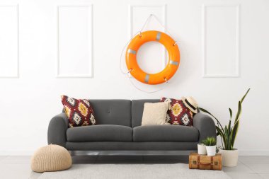 Yastıklı rahat kanepe, puf, bavul, ev bitkileri ve oturma odasında can simidi halkası.