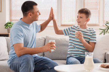 Küçük çocuk ve babası evdeki kanepede birbirlerine beşlik çakıyorlar.