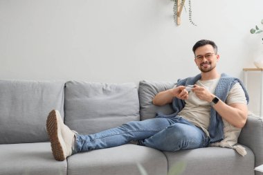 Nabız oksimetresi olan genç adam evdeki kanepede yatıyor.