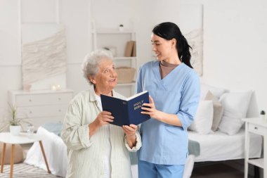 Bakıcı ve kıdemli kadın evde İncil okuyor.