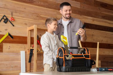 Mutlu baba ve küçük oğlu farklı aletlerle atölyede mobilya montajlıyorlar.