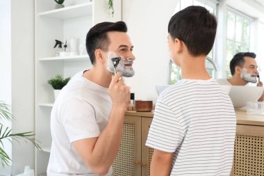 Mutlu baba ve küçük oğlu banyoda tıraş köpüğüyle jilet tutuyorlar.