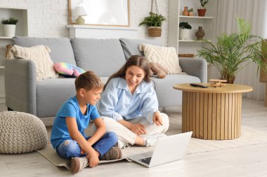 Annesiyle birlikte evde dizüstü bilgisayardan çizgi film izleyen sevimli bir çocuk.