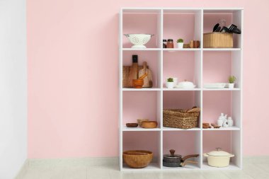 Mutfaktaki pembe duvarın yanında mutfak aletleri olan modern raf ünitesi.