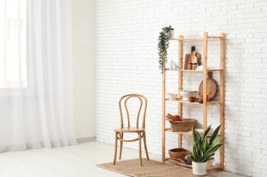 Mutfaktaki beyaz tuğla duvarın yanında mutfak aletleri ve sandalye olan modern raf ünitesi.