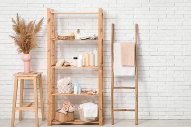 Banyo aksesuarları, otlar ve beyaz tuğla duvarın yanında merdiven olan modern raf ünitesi.