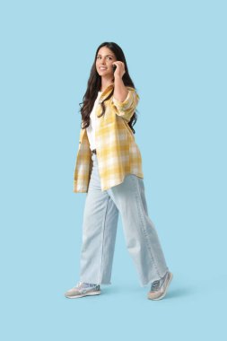 Mavi arka planda telefonla konuşurken yürüyen güzel bir genç kadının portresi.