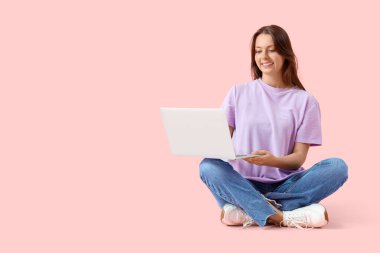 Young woman using laptop on pink background
