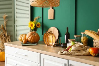 Mutfaktaki yeşil duvarın yanındaki tezgahlarda yemek ve şarap bulunan balkabakları.