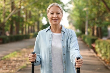 Güzel, olgun, mutlu bir kadın parkta sırıklarla antrenman yapıyor.