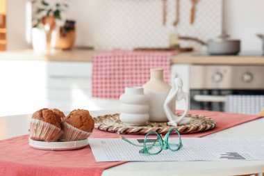 Mutfaktaki yemek masasının üzerinde gazete ve kek olan gözlük, yakın plan.